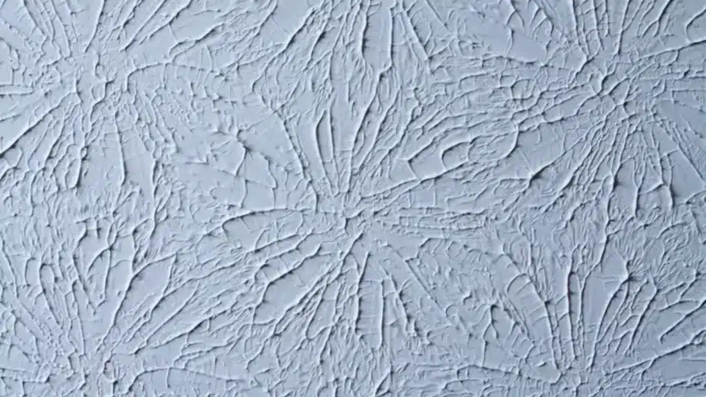 Blue rosebud drywall texture shows flower like stamped patterns with thin raised ridges and deep shadows across a wall
