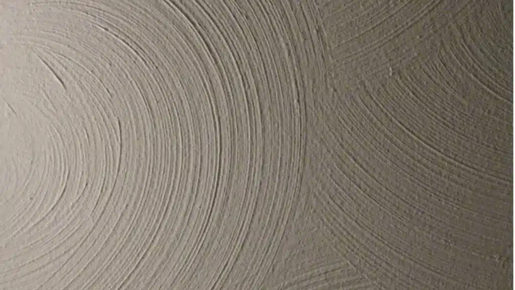 Tan sand swirl drywall texture shows overlapping circular patterns made with a brush on a wall with soft side lighting