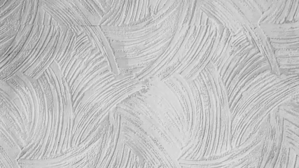 White comb drywall texture shows overlapping arched grooved patterns made with a notched tool on a light colored surface