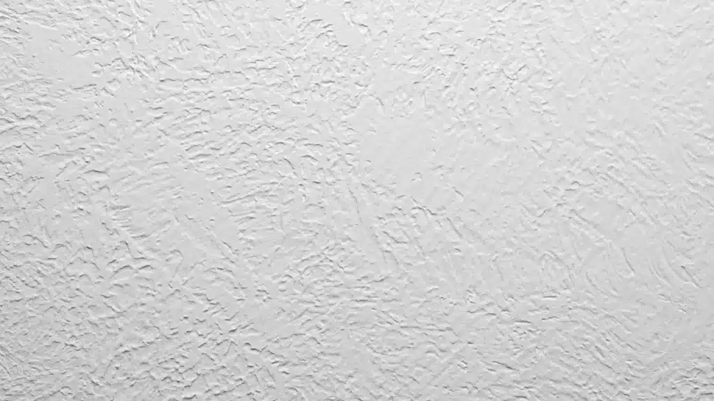 White hawk and trowel drywall texture shows fluid hand applied plaster swirls with flat peaks and soft shadows on a wall
