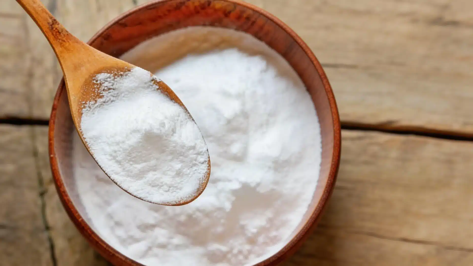 High angle shot of a wooden spoon scooping white powder from a wooden bowl on a rustic wood surface in bright sunlight (1)