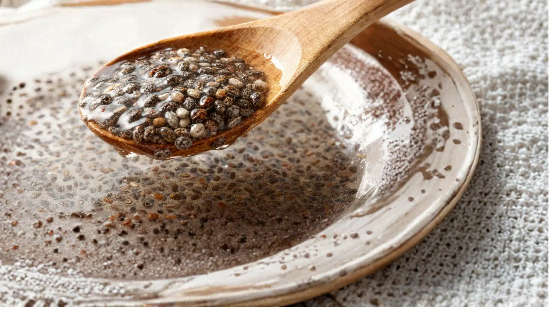 Macro shot of a wooden spoon holding wet chia seeds over a glass bowl filled with more soaking seeds in natural lighting