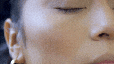 Close-up of smooth, glowing skin on the cheek with natural makeup finish, while highlighting with a brush