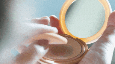 Hands opening a compact powder with a mirror and the other hand dapping it with a powder puff