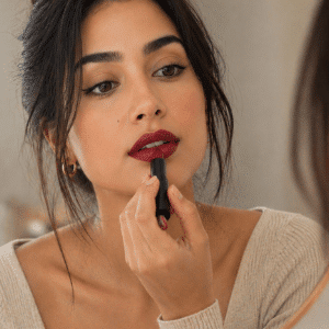 Woman applying bold red lipstick in mirror with soft lighting and minimal makeup look