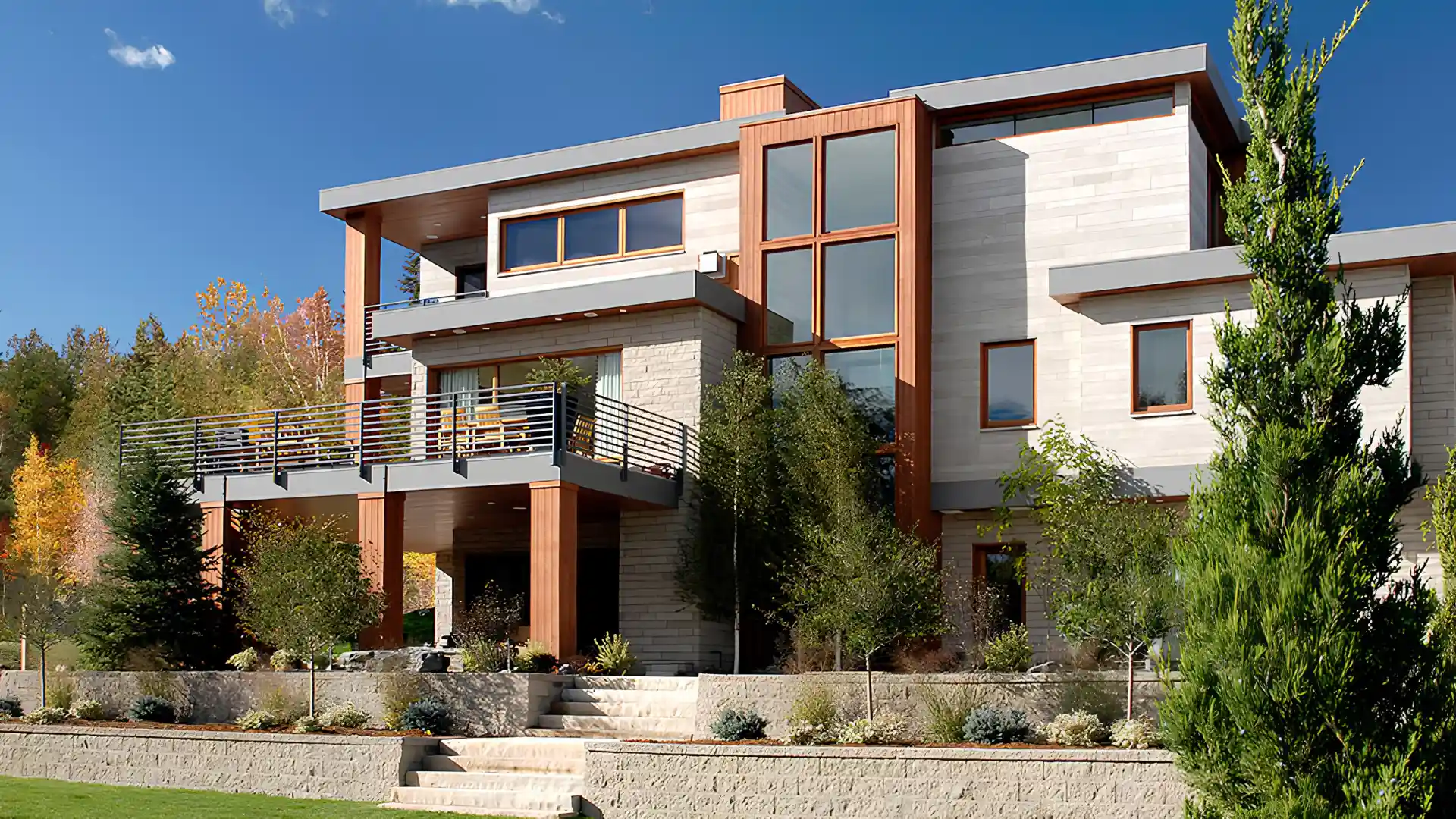 Modern multi story custom house with stone and wood facade and large windows surrounded by trees